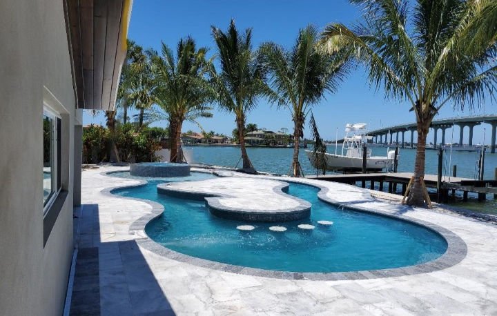 Waterfront freeform pool with raised spa and stepping stones by CAM Pool Projects